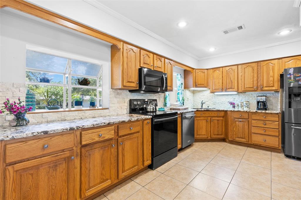 A kitchen with oak cabinets, granite countertops, black appliances, and light-colored tile flooring — 1950 REBECCA DRIVE, CLEARWATER, FL