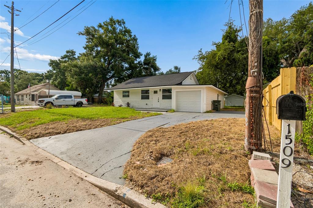 A single-story white house with a garage and a driveway sits on a grassy lot — 1509 15TH AVE W, BRADENTON, FL