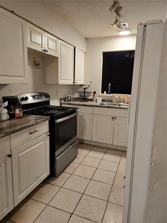 A kitchen features white cabinets, a stainless steel stove, and light-colored tile flooring — 572 MAINELINE BOULEVARD, APOPKA, FL