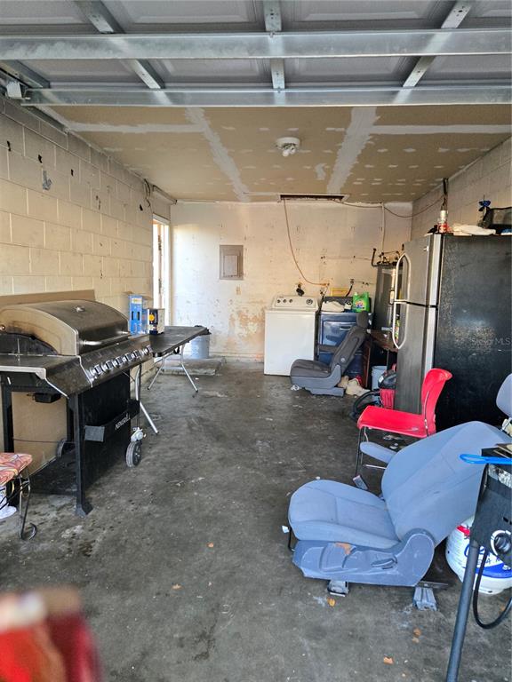 A cluttered garage with concrete block walls, a concrete floor, and a washer — 572 MAINELINE BOULEVARD, APOPKA, FL