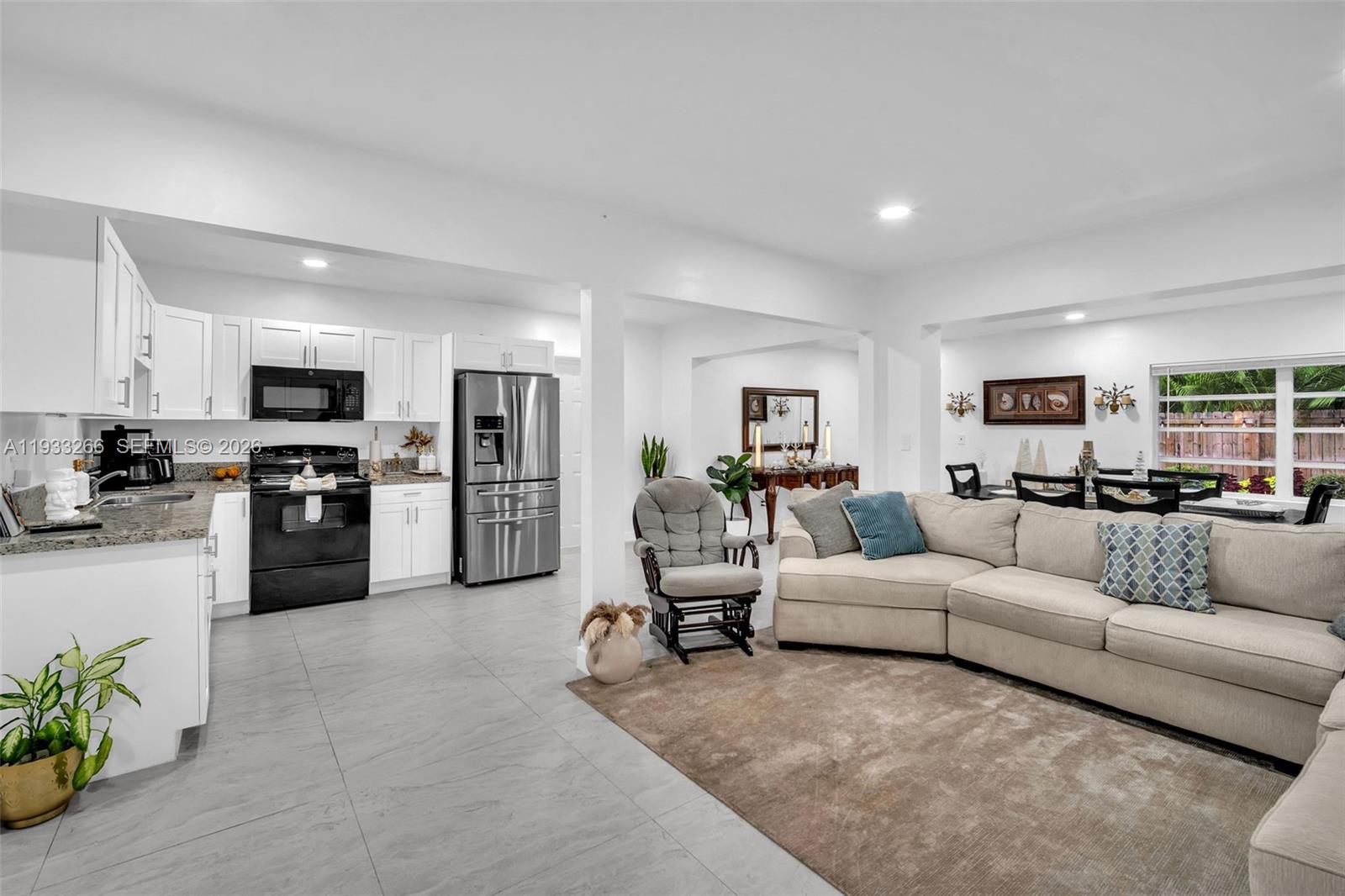 An open-concept kitchen and living area features white cabinetry, stainless steel appliances, and tile flooring — 14140 NE 10th Ave, North Miami FL 33161, NORTH MIAMI, FL