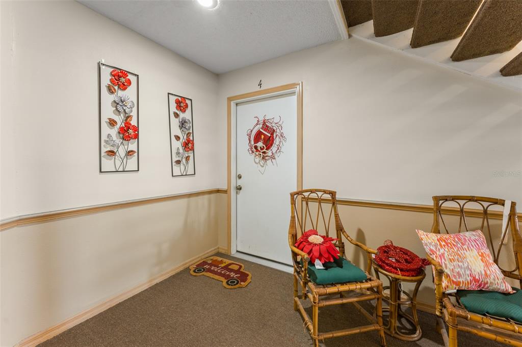 An entryway features a white door, two wicker chairs, wall art, and a welcome mat — 5300 DOVER VILLAGE LANE UNIT 4, ORLANDO, FL