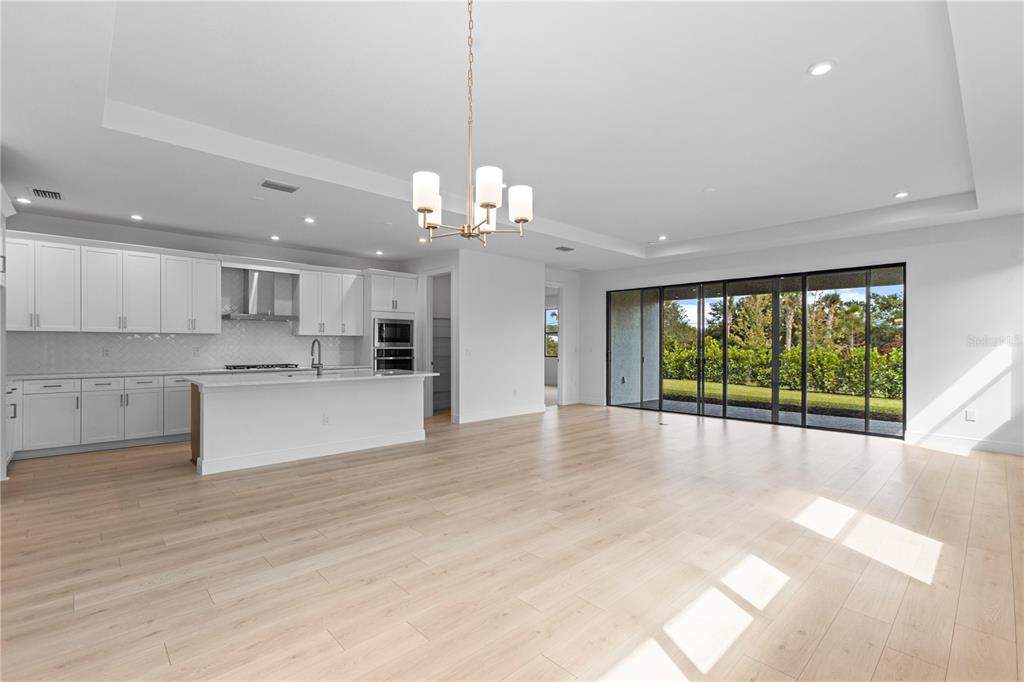 A modern kitchen with white cabinetry and an island opens to a spacious living area — 5032 LOWLAND TERRACE, PARRISH, FL