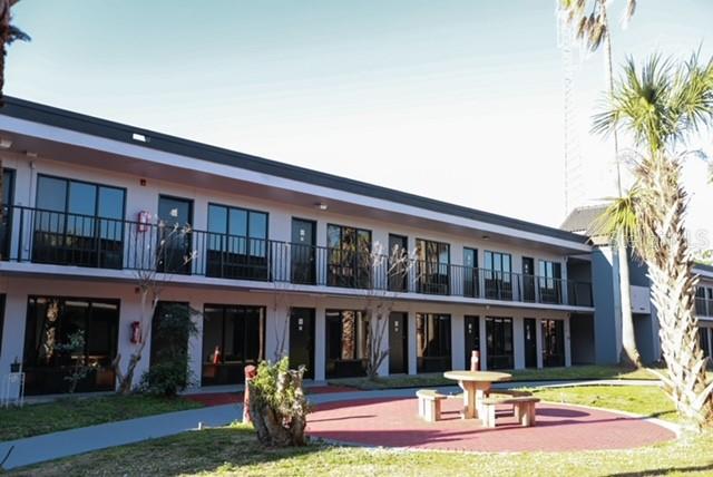 A two-story motel building with exterior walkways, black railings, and a central outdoor seating area — 8421 S ORANGE BLOSSOM TRAIL UNIT 436, ORLANDO, FL