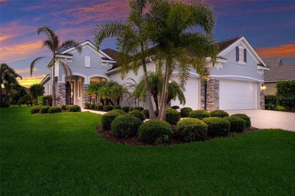 A single-story house with a light blue exterior, stone accents, and a manicured front lawn — 12825 COASTAL BREEZE WAY, BRADENTON, FL