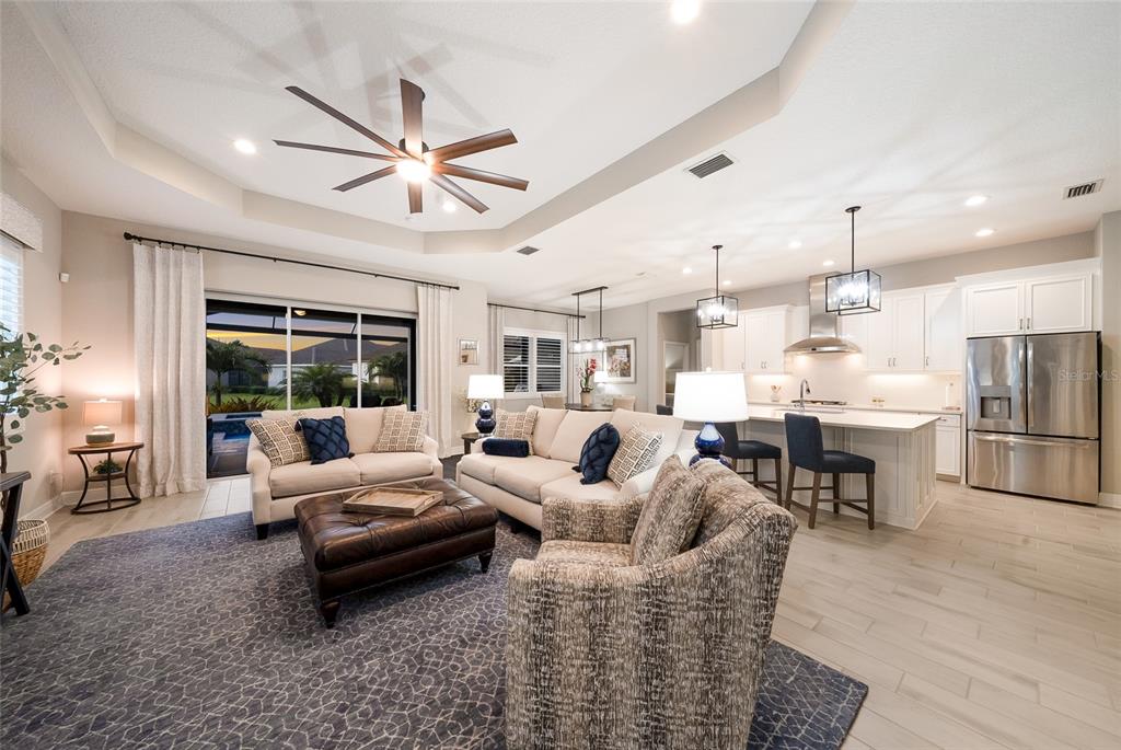 An open-concept living room and kitchen feature a tray ceiling, ceiling fan, and tile flooring — 12825 COASTAL BREEZE WAY, BRADENTON, FL