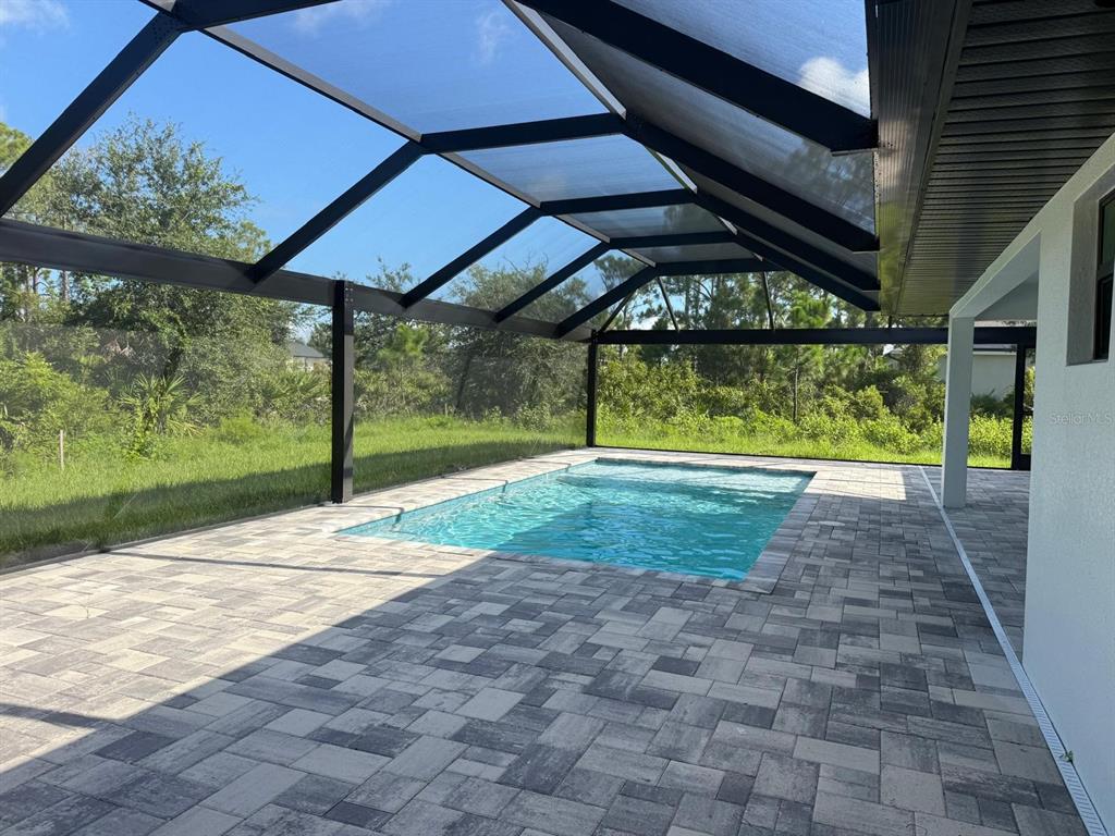 A rectangular swimming pool sits on a paved patio enclosed by a black screen cage — 8285 AGATE STREET, PORT CHARLOTTE, FL
