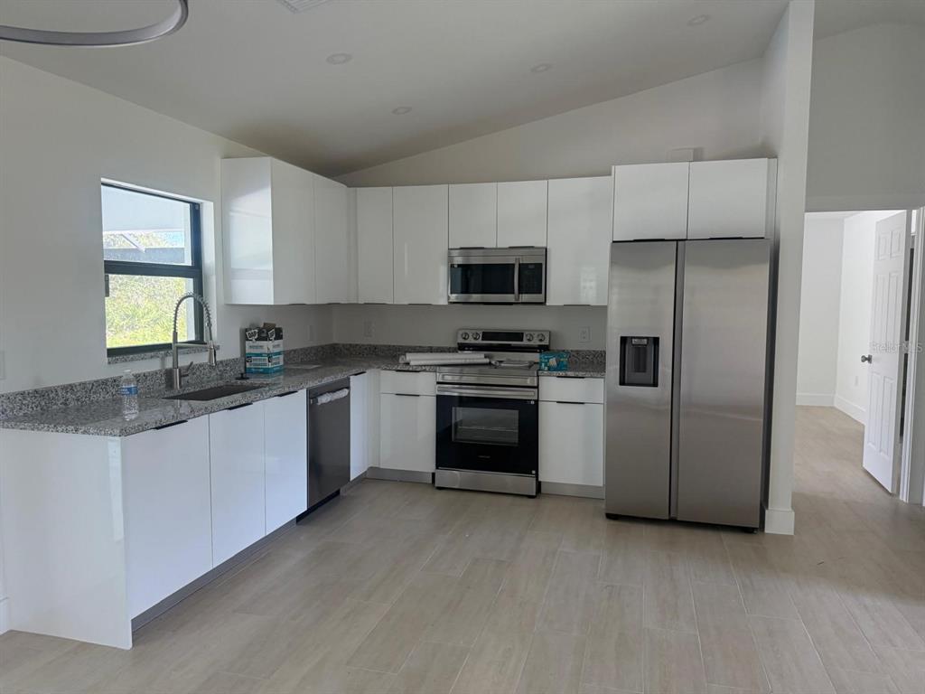 A modern kitchen features white cabinets, granite countertops, stainless steel appliances, and light-colored tile flooring — 8285 AGATE STREET, PORT CHARLOTTE, FL