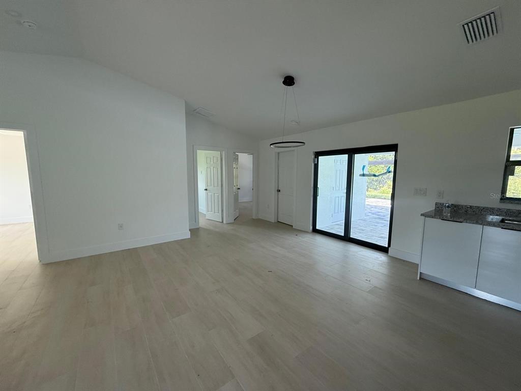 An open-concept room features light wood flooring, white walls, a modern pendant light, and sliding doors — 8285 AGATE STREET, PORT CHARLOTTE, FL