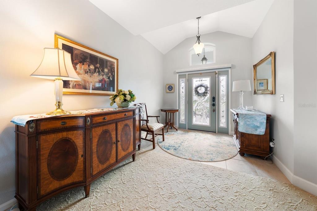 A bright foyer features a vaulted ceiling, a wooden sideboard, and a glass-paneled front door — 2218 DONATO DRIVE, BELLEAIR BEACH, FL