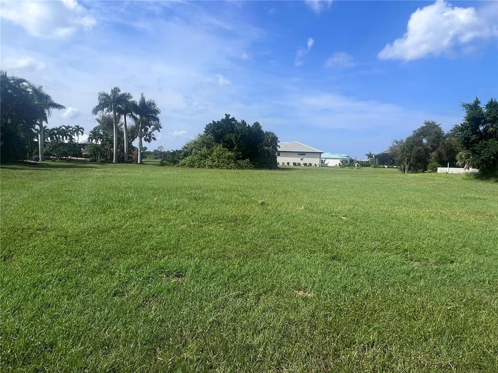 A large, grassy vacant lot features scattered trees and distant houses under a blue sky — 24183 SANTA INEZ ROAD, PUNTA GORDA, FL