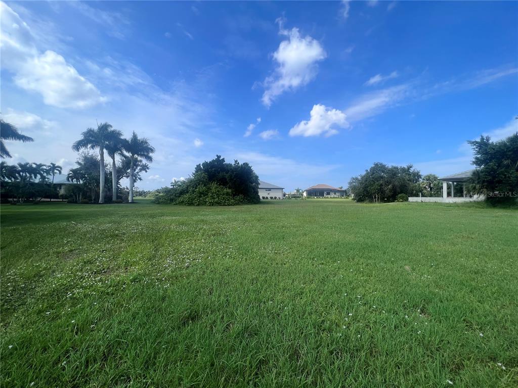 A large, grassy vacant lot features scattered trees and distant houses under a blue sky — 24183 SANTA INEZ ROAD, PUNTA GORDA, FL