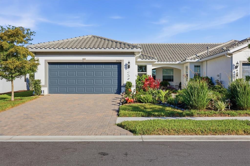 A single-story house with a blue garage door, tiled roof, and a paved driveway — 25029 PEARL LAKE CIRCLE, ENGLEWOOD, FL