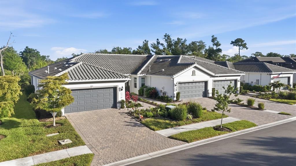 An aerial view shows two attached single-story houses with gray tile roofs and paver driveways — 25029 PEARL LAKE CIRCLE, ENGLEWOOD, FL