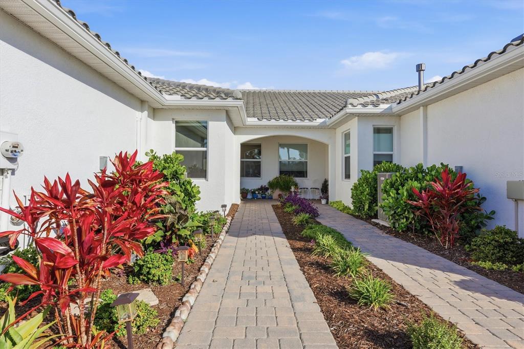 A paved walkway leads to the recessed entryway of a white house with landscaping — 25029 PEARL LAKE CIRCLE, ENGLEWOOD, FL