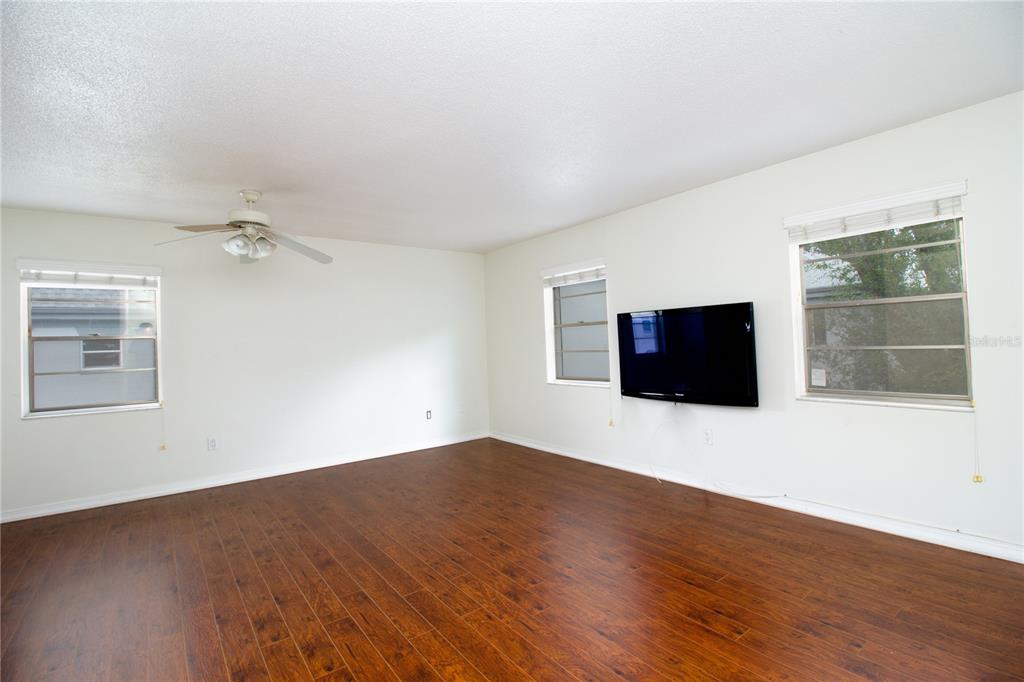 An empty living room with dark wood flooring, white walls, a ceiling fan, and a television — 6940 SUNSET DRIVE S UNIT 2C, ST PETERSBURG, FL
