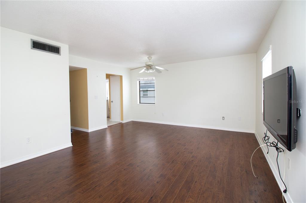 An empty living room features dark wood-look flooring, white walls, a ceiling fan, and television — 6940 SUNSET DRIVE S UNIT 2C, ST PETERSBURG, FL
