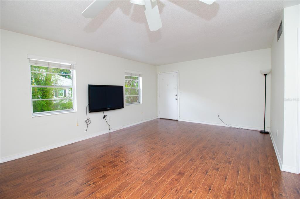 A living room with wood-look flooring, a wall-mounted television, and a white ceiling fan — 6940 SUNSET DRIVE S UNIT 2C, ST PETERSBURG, FL