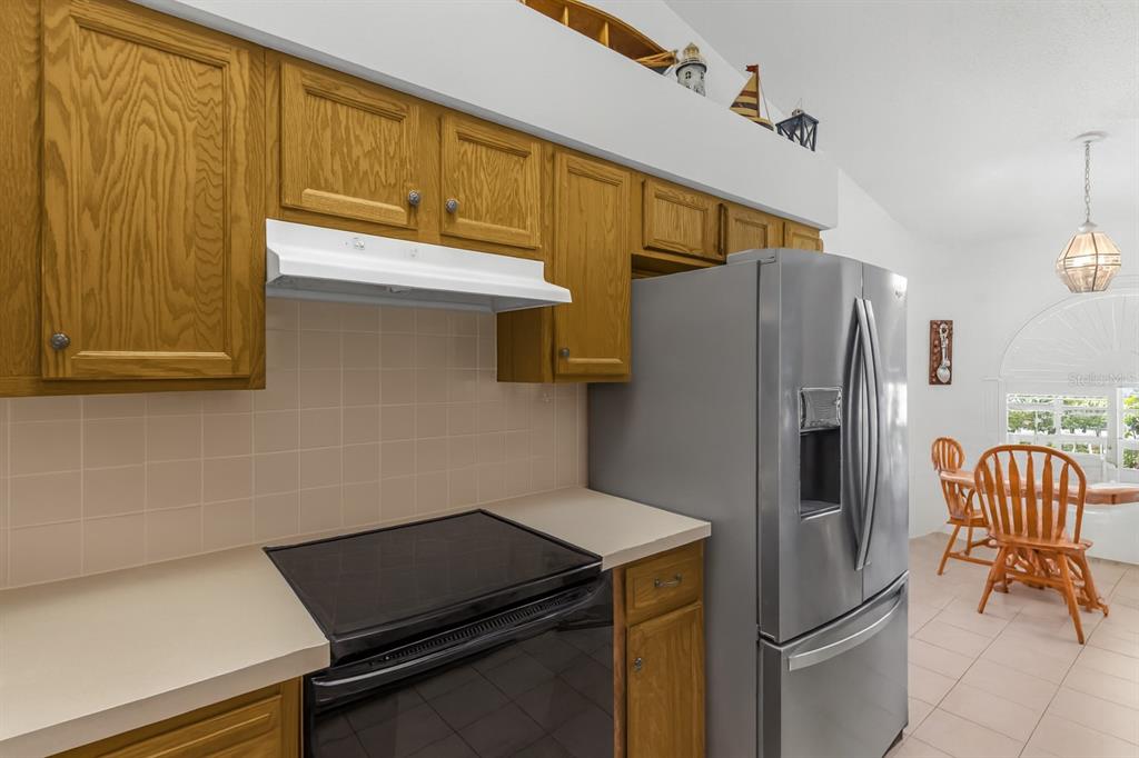 A kitchen features oak cabinets, a stainless steel refrigerator, and a black electric range — 1237 FRANFORD DRIVE, BRANDON, FL