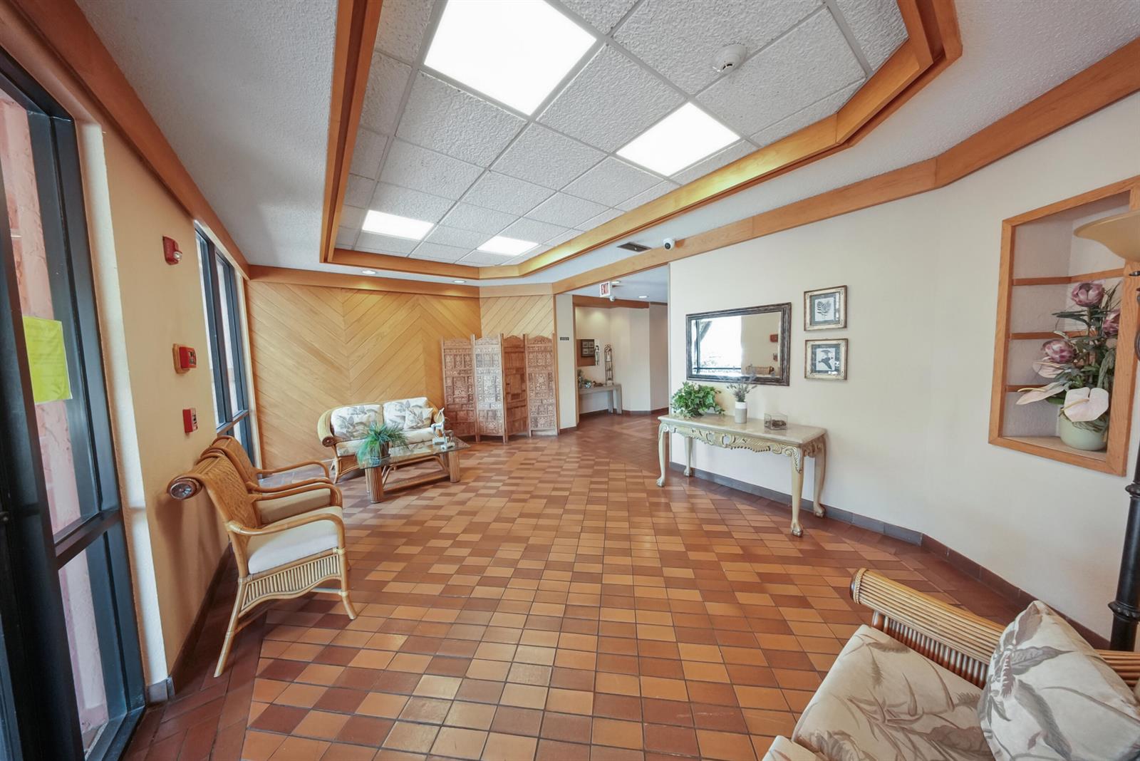 A waiting area features a tiled floor, wood-paneled walls, wicker furniture, and a console table — 20860 San Simeon Way # 6, Miami FL 33179, MIAMI, FL
