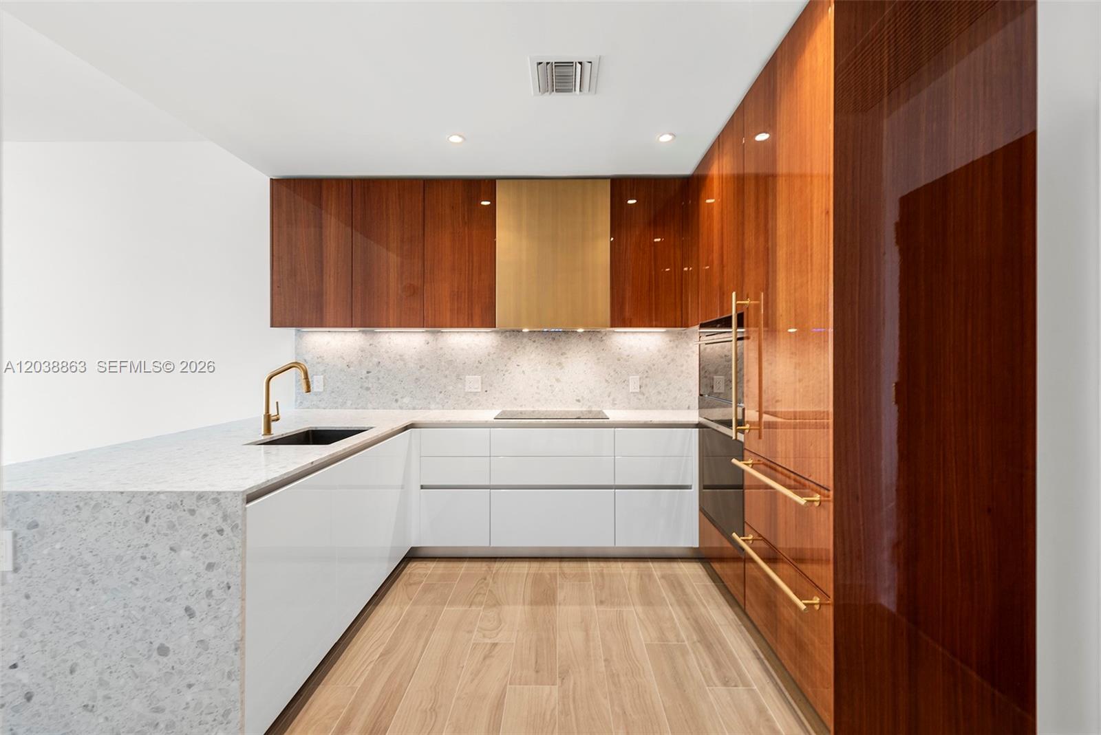 A modern kitchen features white lower cabinets, wood-veneer upper cabinets, and a speckled stone countertop — 2678 Tigertail Ave # 1005, Miami FL 33133, MIAMI, FL