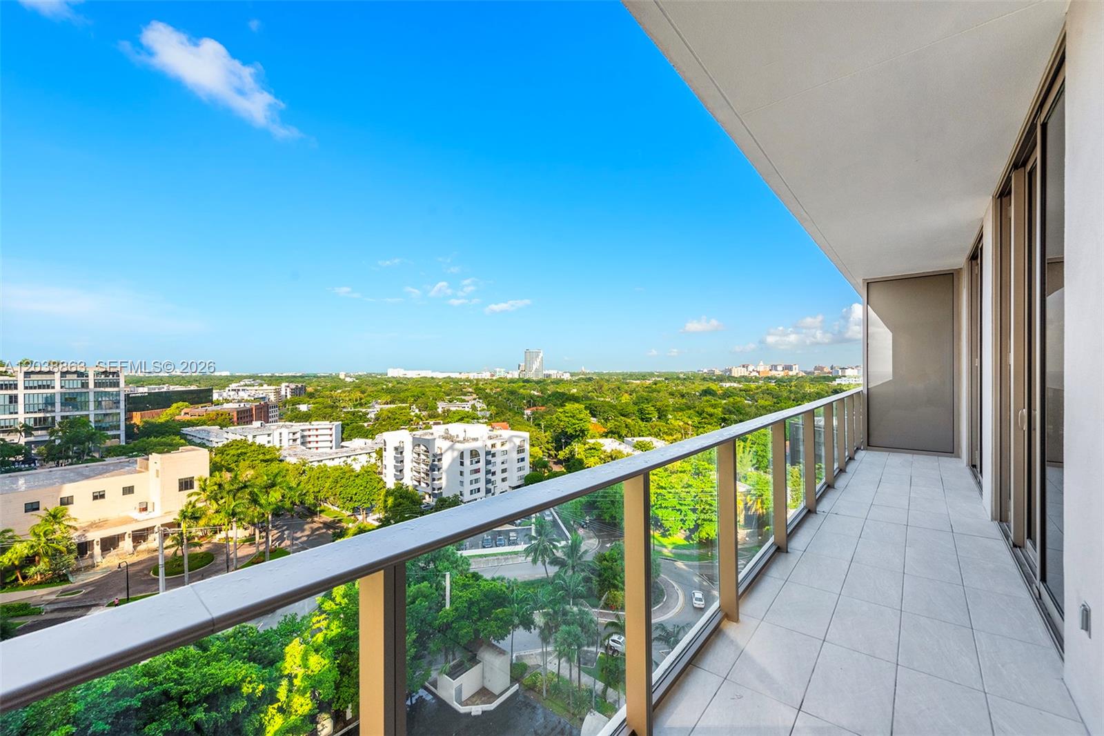 A high-rise balcony with a glass railing overlooks a lush green city landscape — 2678 Tigertail Ave # 1005, Miami FL 33133, MIAMI, FL