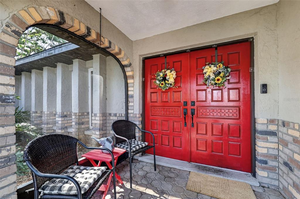 A covered porch features a red double door, two wicker chairs, and brick accents — 2713 WILLOW OAKS DRIVE, VALRICO, FL