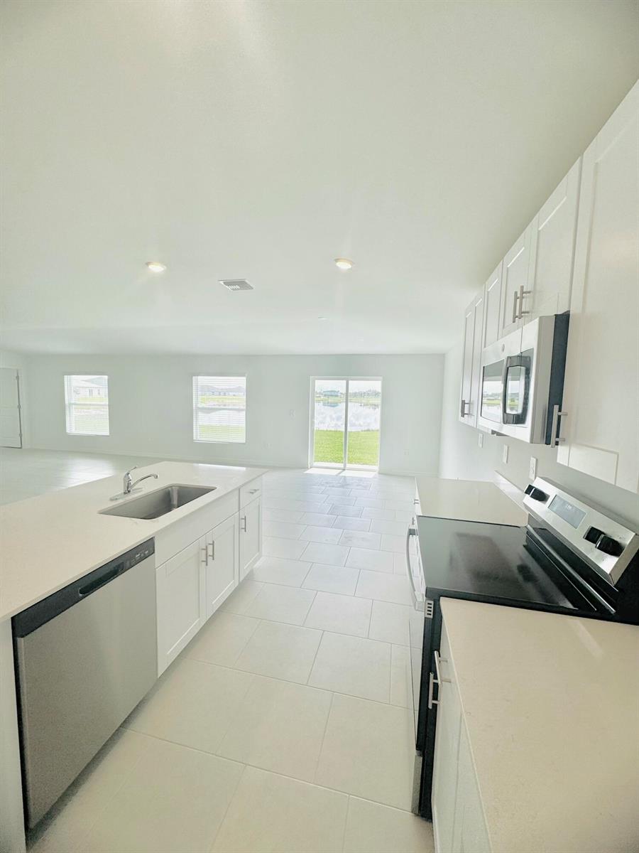 A modern kitchen features white cabinets, stainless steel appliances, and a central island with sink — 17124 Pompeii Way, FL 33917, FL