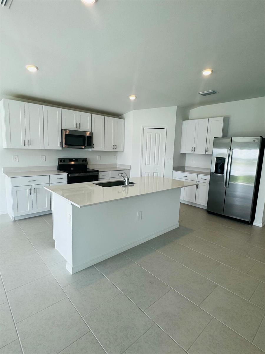 A kitchen features white cabinets, stainless steel appliances, a center island, and light tile flooring — 17124 Pompeii Way, FL 33917, FL