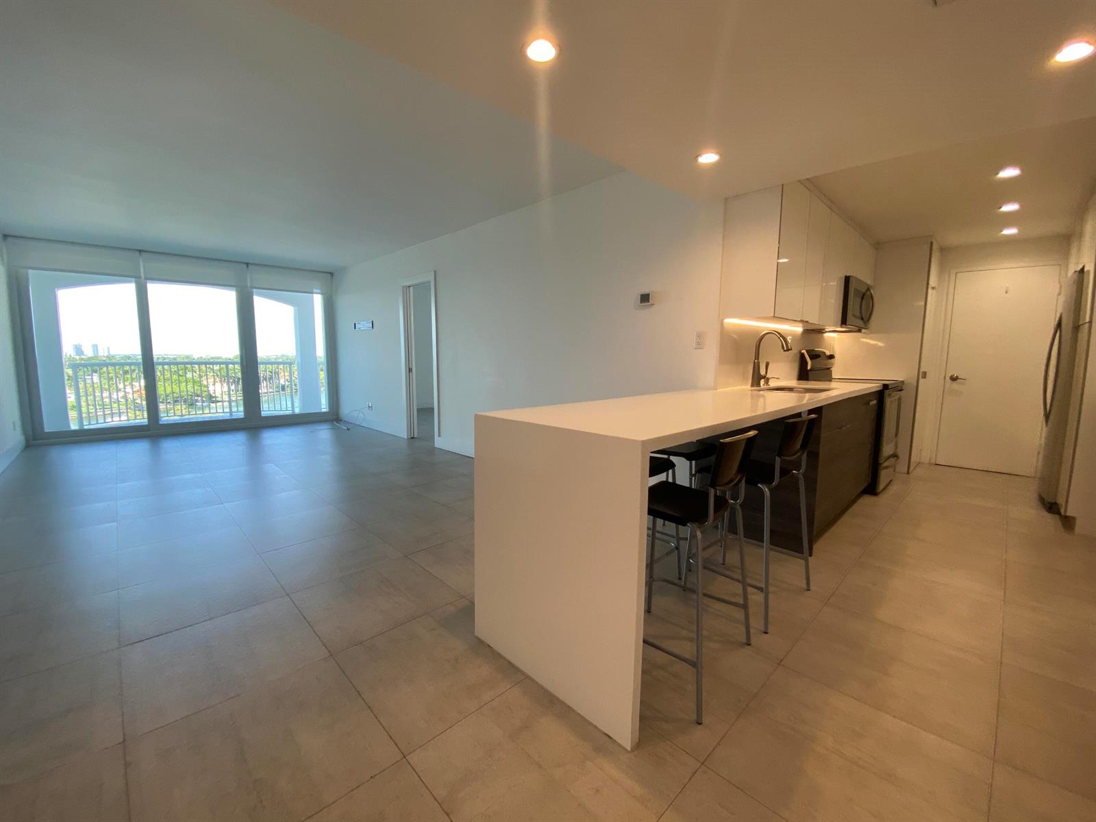 An open-concept kitchen with a white waterfall island overlooks a living area with balcony access — 5401 Collins Avenue # 620, Miami Beach FL 33140, MIAMI BEACH, FL