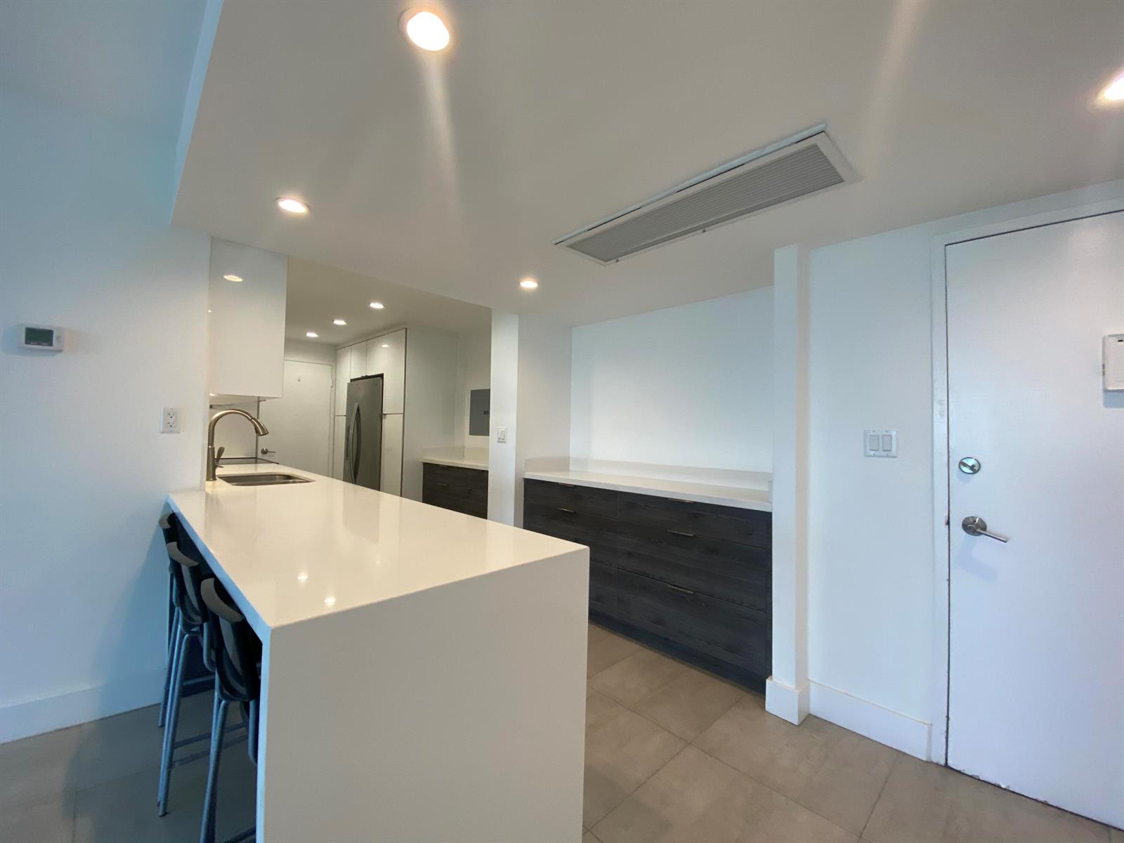 A modern kitchen features a white quartz island, dark wood cabinetry, and light tile flooring — 5401 Collins Avenue # 620, Miami Beach FL 33140, MIAMI BEACH, FL