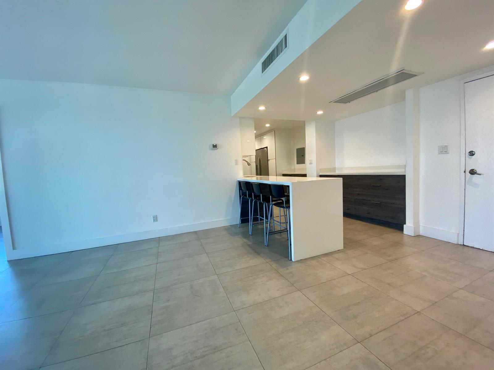 A modern kitchen features a white island with bar stools and dark wood cabinetry — 5401 Collins Avenue # 620, Miami Beach FL 33140, MIAMI BEACH, FL