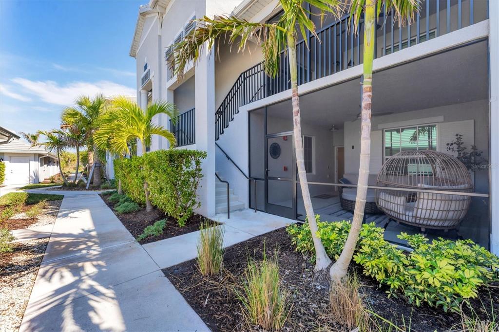 A ground-floor screened patio with a hanging chair sits beside a staircase and landscaping — 14184 HERITAGE LANDING BOULEVARD UNIT 516, PUNTA GORDA, FL