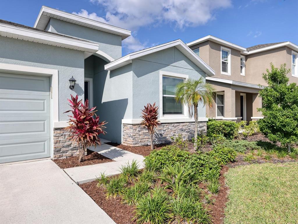 A light blue house with a stone-accented facade, a garage, and a landscaped front yard — 17605 CANTARINA COVE, BRADENTON, FL