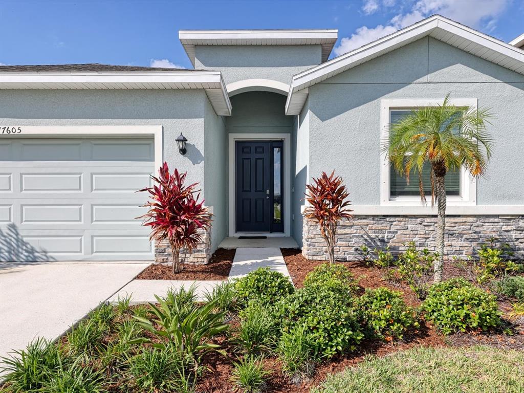 A light blue house exterior features a dark blue front door, stone accents, and landscaping — 17605 CANTARINA COVE, BRADENTON, FL