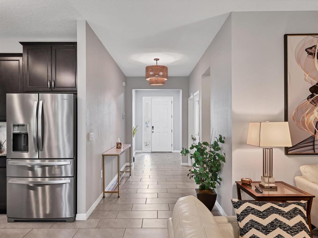 A hallway with tile flooring leads to a white front door under a woven light fixture — 17605 CANTARINA COVE, BRADENTON, FL