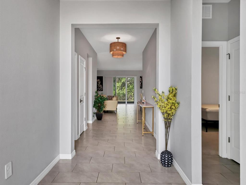 A tiled hallway leads to a living area with a wicker chandelier and sliding doors — 17605 CANTARINA COVE, BRADENTON, FL