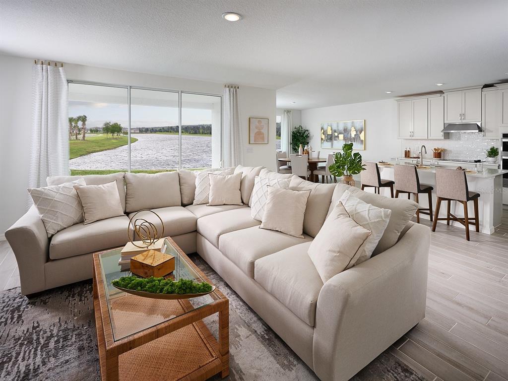A bright open-concept living room features a large sectional sofa overlooking a scenic lake view — 3910 NATURE SOUND LANE, BARTOW, FL