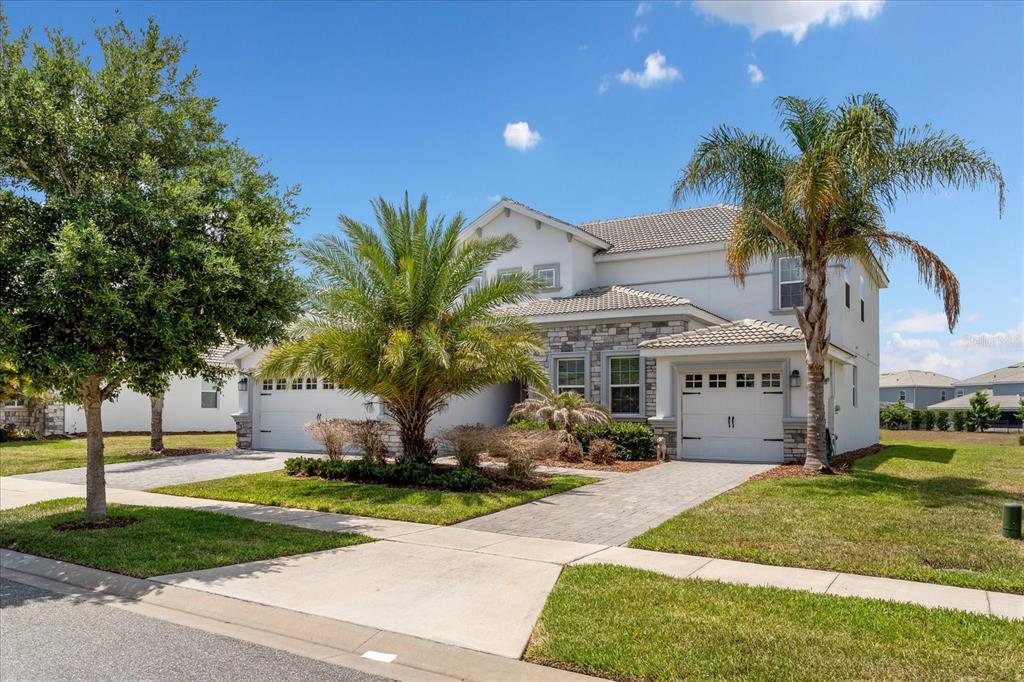 A two-story house with a stone facade, two garages, and palm trees in the front yard — 1432 OLYMPIC CLUB BOULEVARD, CHAMPIONS GATE, FL