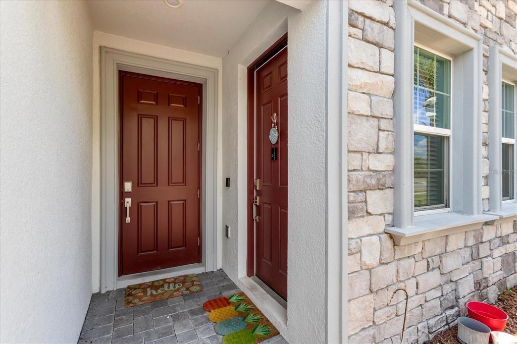 A covered entryway features two red doors, stone veneer siding, and a paved floor — 1432 OLYMPIC CLUB BOULEVARD, CHAMPIONS GATE, FL