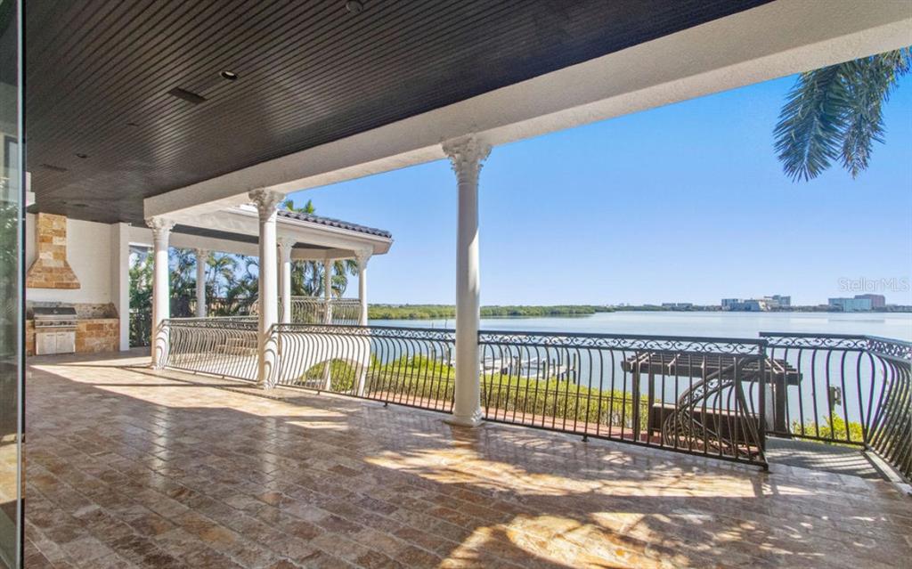 A covered stone patio features white columns, a black ceiling, and a metal railing overlooking water — 4107 CAUSEWAY VISTA DRIVE, TAMPA, FL