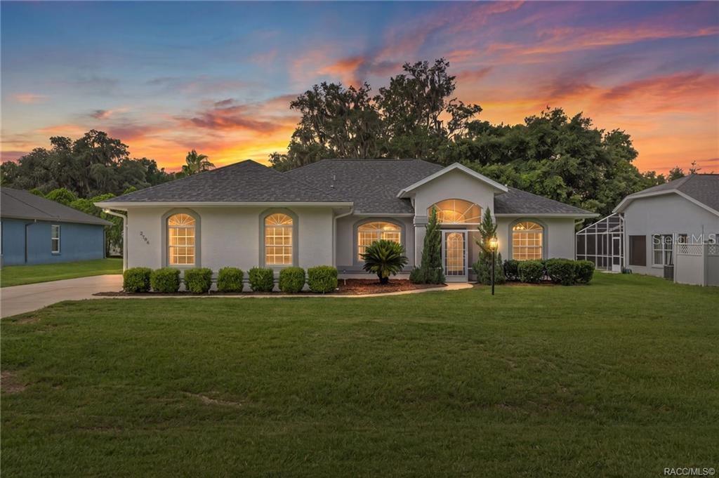 A single-story house with a white stucco exterior and a gray roof at sunset — 2786 N CANTERBURY LAKE DRIVE, HERNANDO, FL