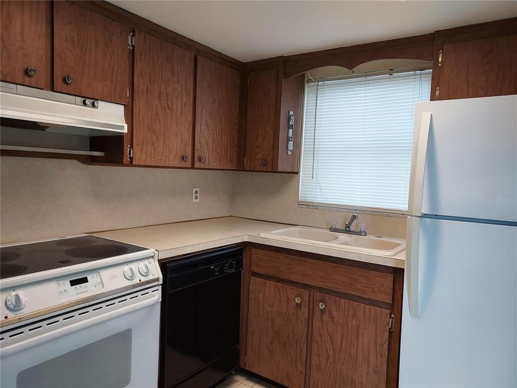 A kitchen features wood cabinets, a white stove, a black dishwasher, and a double sink — 1240 CHELSEA LANE, HOLIDAY, FL