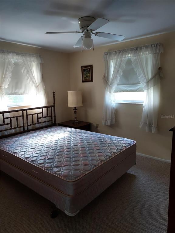 A bedroom features a mattress on a wooden frame, a bedside lamp, and two windows — 1240 CHELSEA LANE, HOLIDAY, FL