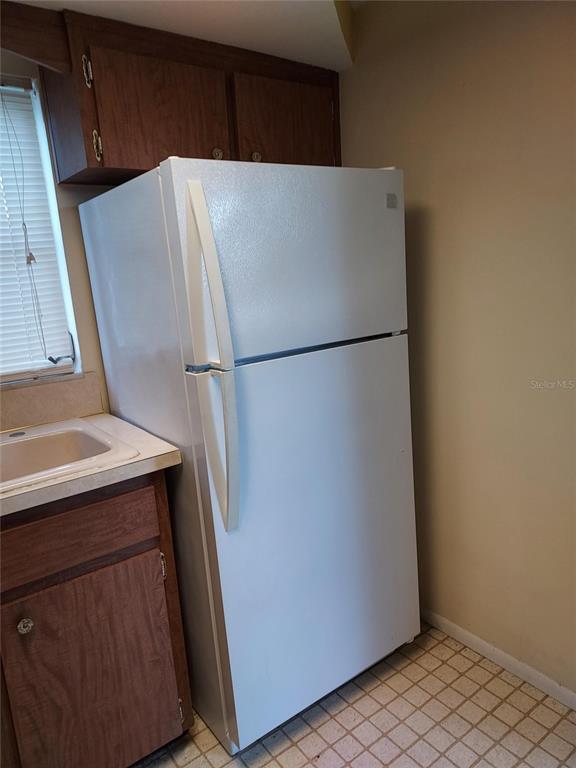 A white top-freezer refrigerator stands next to a kitchen sink and wooden cabinets — 1240 CHELSEA LANE, HOLIDAY, FL