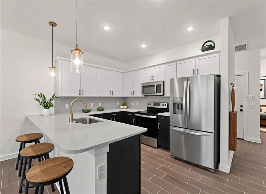 A modern kitchen features white upper cabinets, black lower cabinets, stainless steel appliances, and island seating — 14449 & 14451 APPLETON BOULEVARD, PORT CHARLOTTE, FL