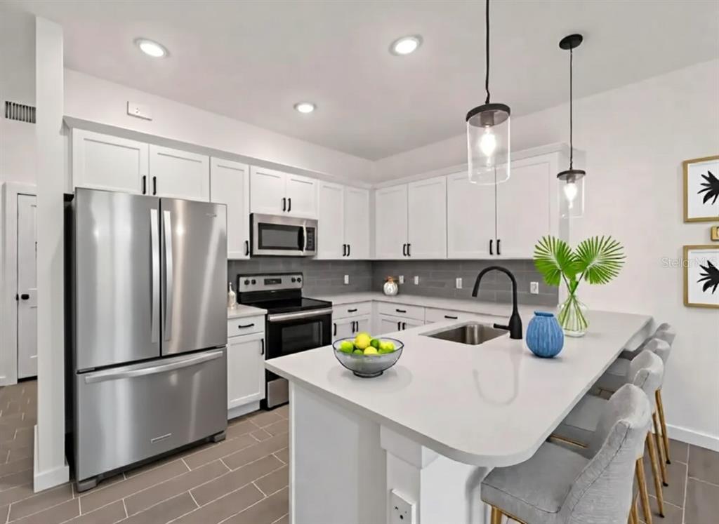 A modern kitchen features white cabinets, stainless steel appliances, a gray backsplash, and a quartz island — 14449 & 14451 APPLETON BOULEVARD, PORT CHARLOTTE, FL
