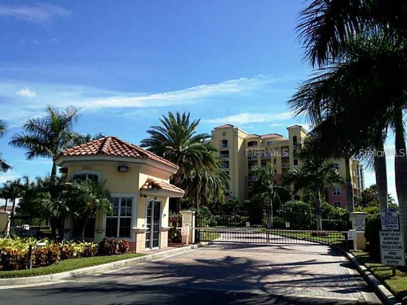 A gated entrance with a guardhouse leads to a multi-story residential building surrounded by palms — 611 RIVIERA DUNES WAY UNIT 604, PALMETTO, FL