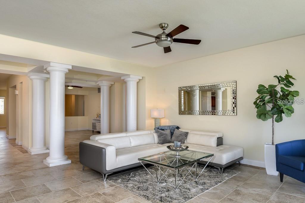 A living room features a white sectional sofa, glass coffee table, columns, and tile flooring — 611 RIVIERA DUNES WAY UNIT 604, PALMETTO, FL