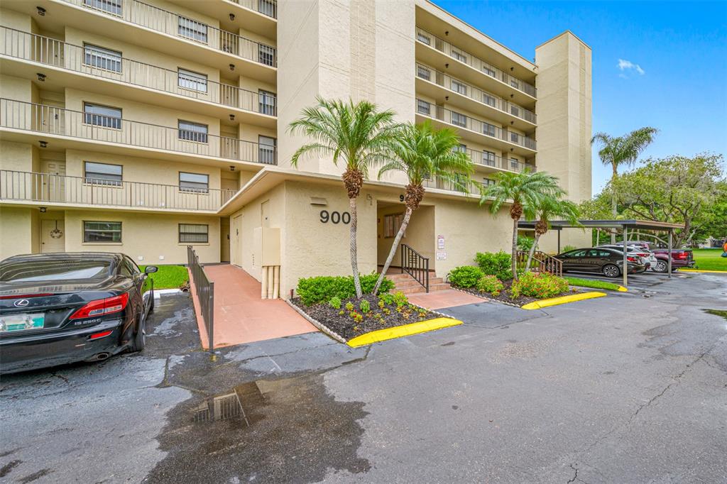 A multi-story apartment building exterior features a covered entrance, palm trees, and parking spaces — 900 COVE CAY DRIVE UNIT 1F, CLEARWATER, FL
